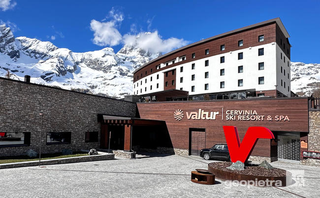 View of Valtur Cervinia Ski Resort & Spa with snow-capped mountains in the background, facade clad in manufactured Geopietra stone, and wooden planks